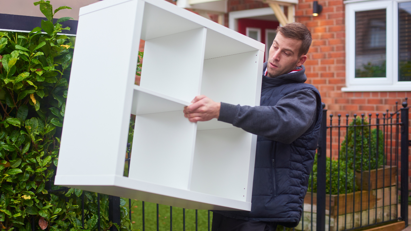 A man is carrying a white shelf in front of a house.