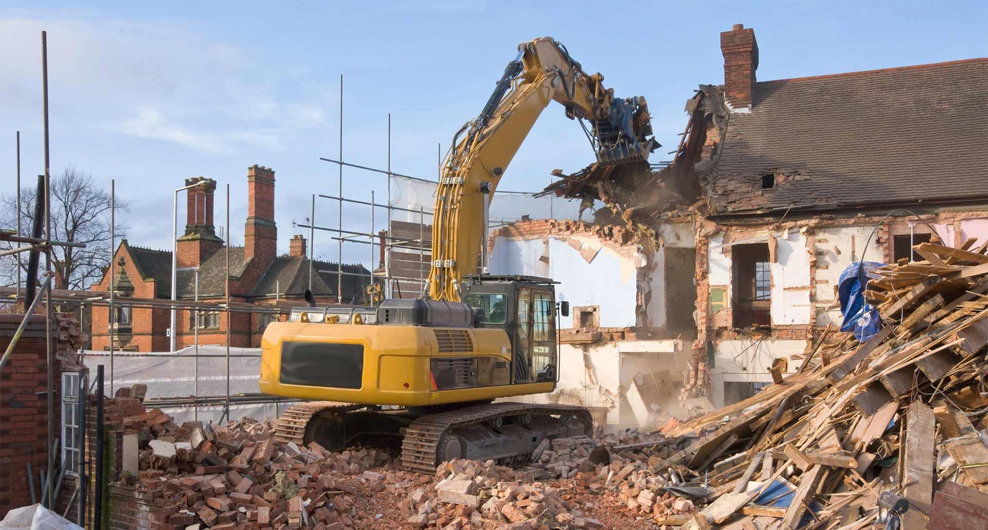 A yellow excavator is demolishing a brick building. - concrete demolition commack