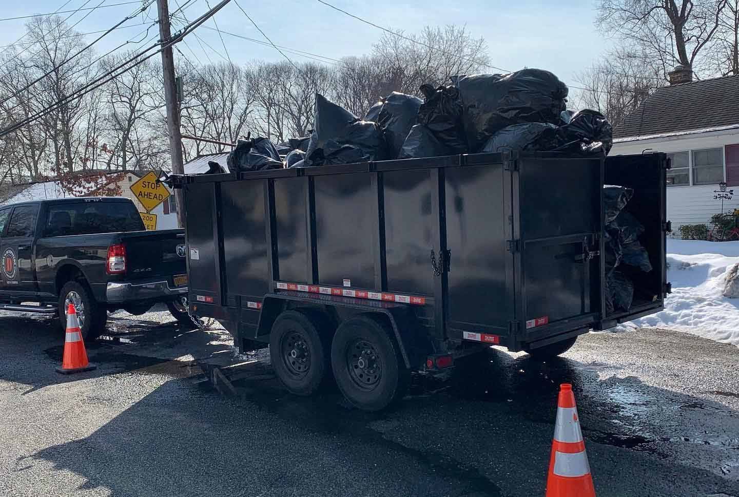 A dumpster trailer filled with trash bags is parked on the side of the road. - dumpster rental