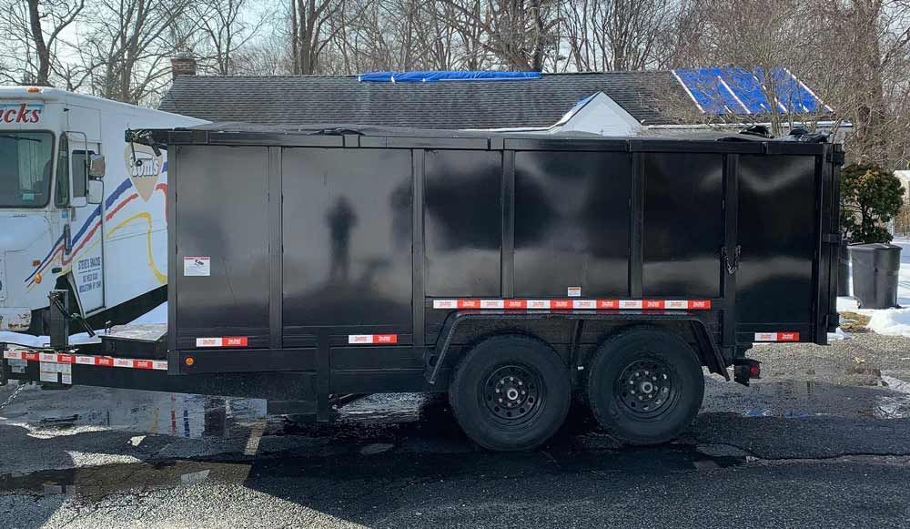 A dumpster trailer is parked in a parking lot next to a truck. - dumpster rental