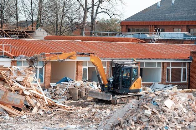 An excavator is destroying a building with a pile of rubble in front of it. - demolition contractor long island