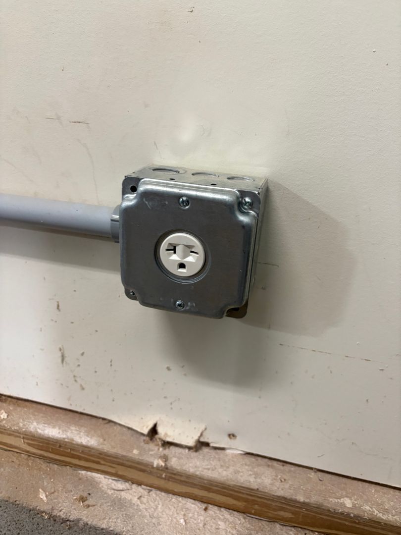 Electrical conduit entering a gray metal wall outlet box with a white receptacle.