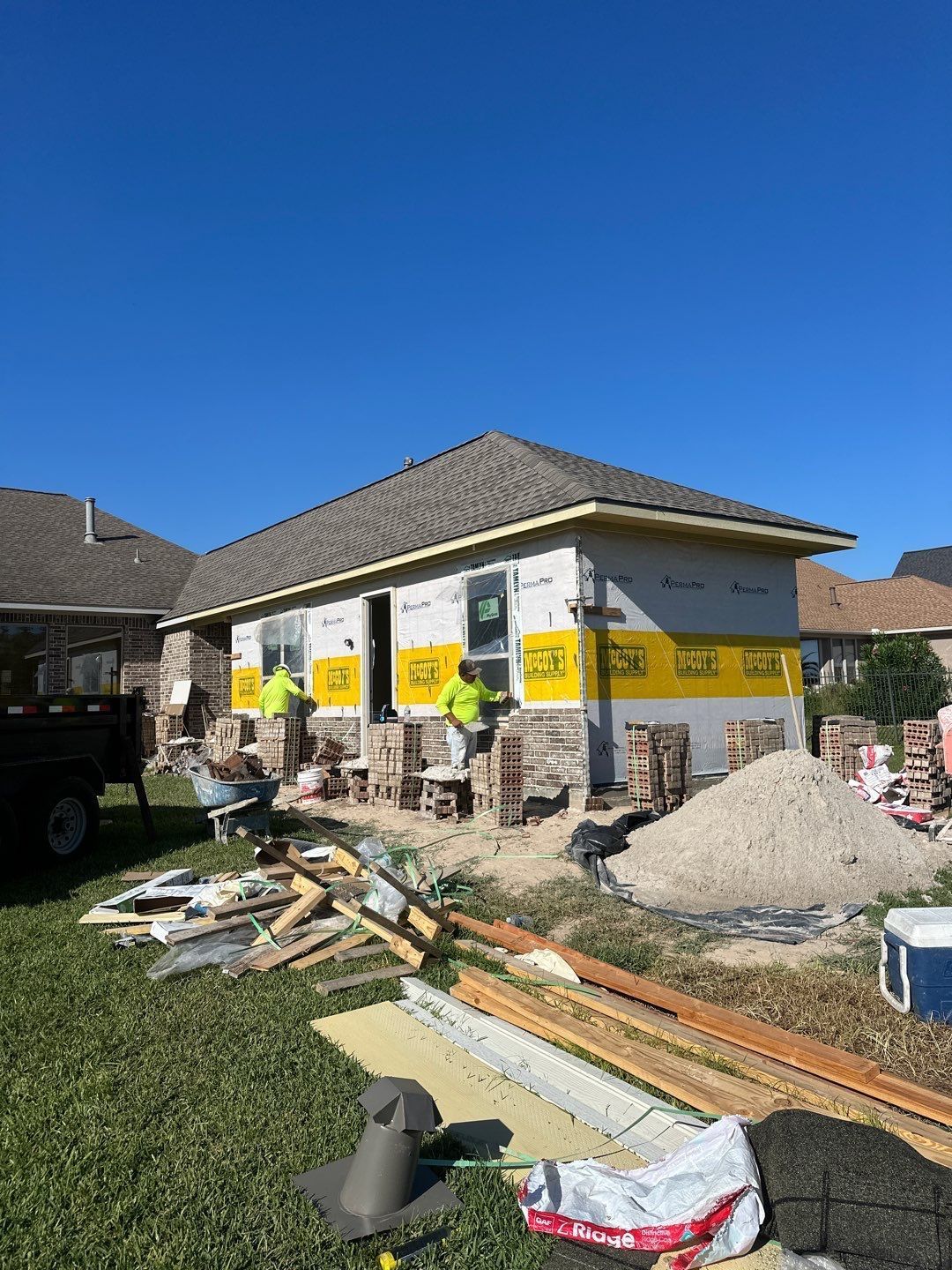 Construction workers at a house foundation repair. Workers in yellow vests. Brick, lumber, and sand visible.