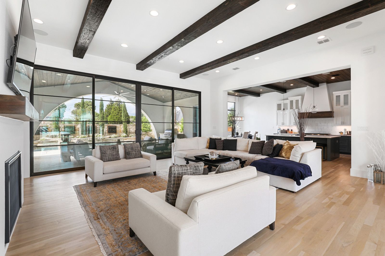 An inviting living room with cream sofas, wooden beams on the ceiling, and large glass windows offering views of an outdoor pool, reflecting PentaVia's remodeling expertise.
