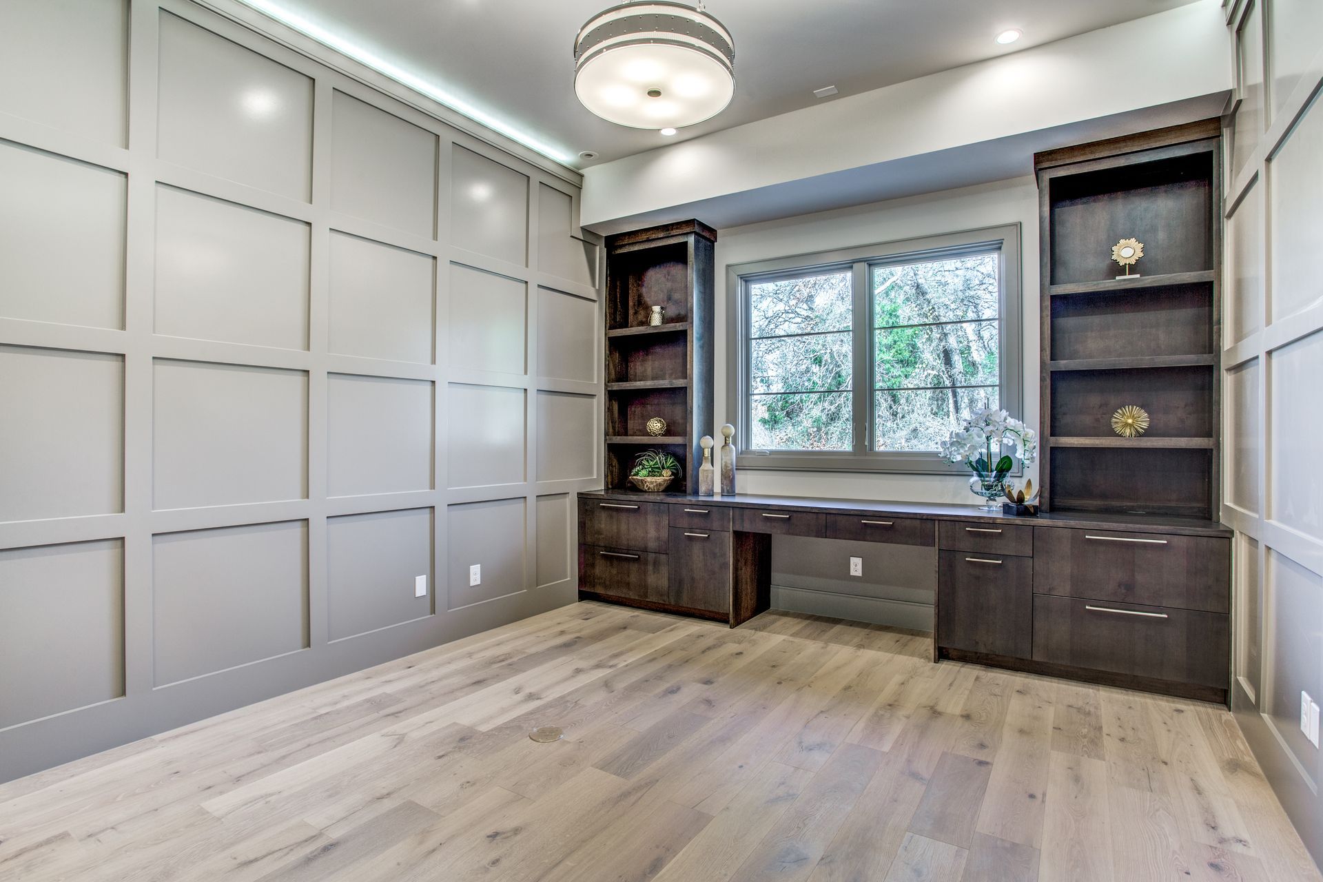 An elegant room showcasing the Five Roads of Design with a stylish wooden floor, paneled walls, and a window framed by a dark wooden bookcase and desk.
