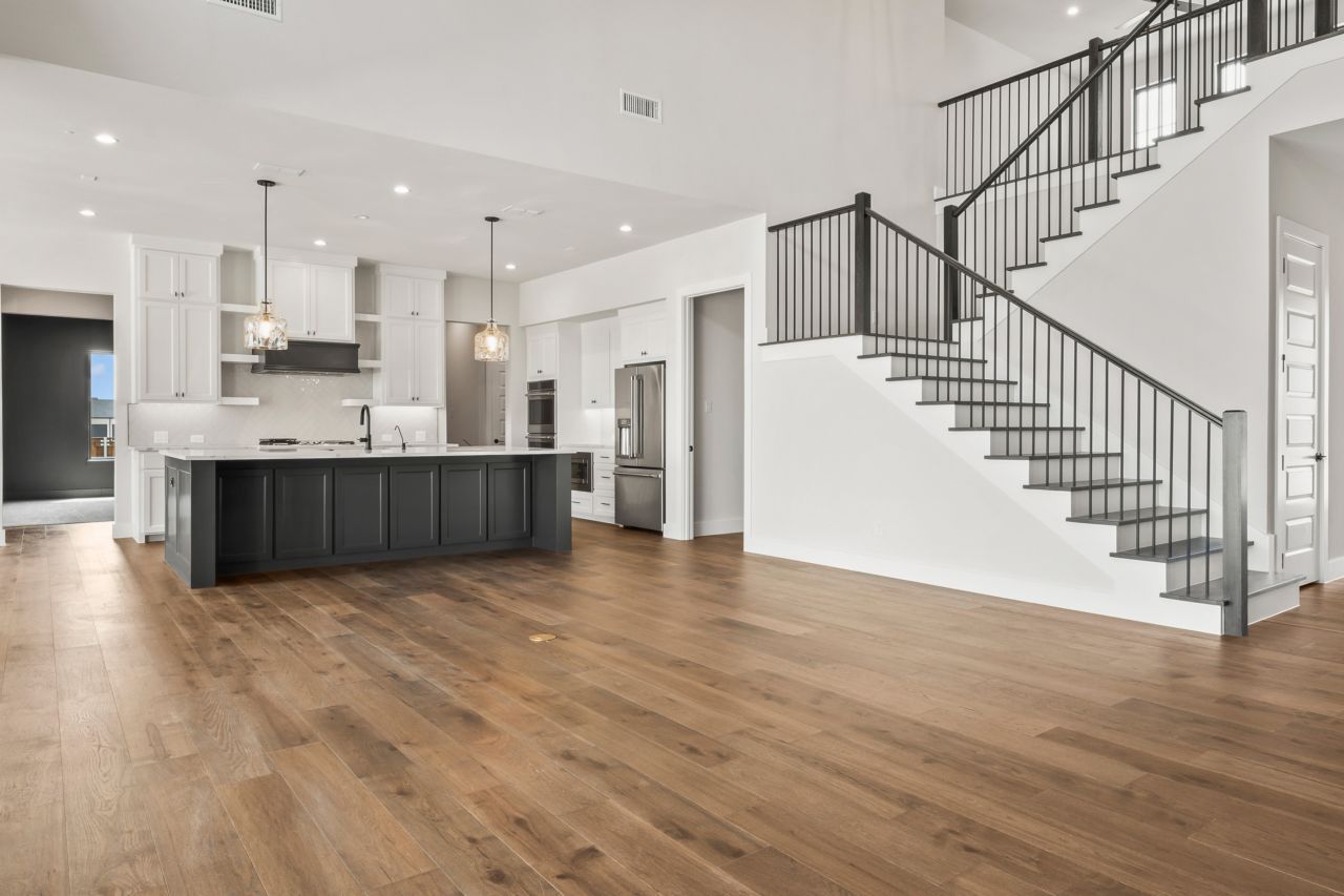 Spacious kitchen and staircase area in a modern home with hardwood floors and white interior.