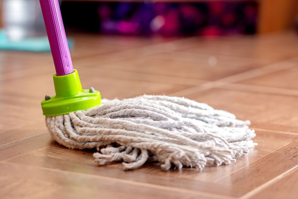 A Mop with A Purple Handle Is Sitting on A Wooden Floor — North Coast Commercial Cleaners In Nambour, QLD