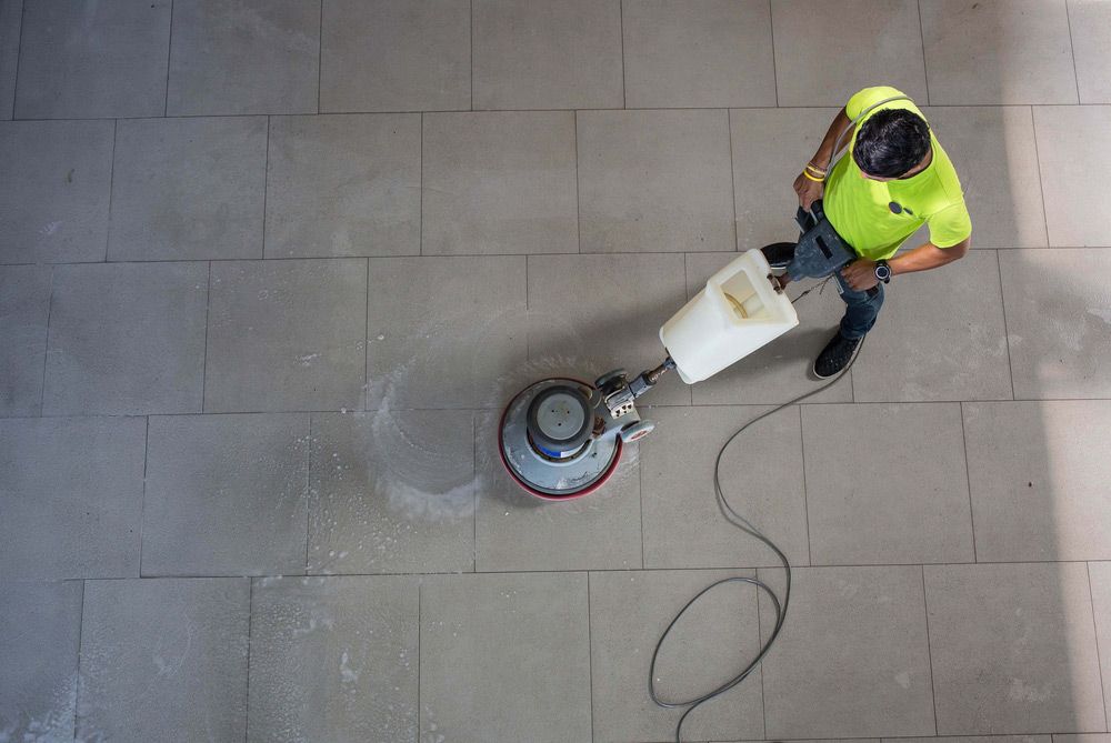 A Man Is Cleaning a Tiled Floor with A Machine — North Coast Commercial Cleaners In Bli Bli, QLD