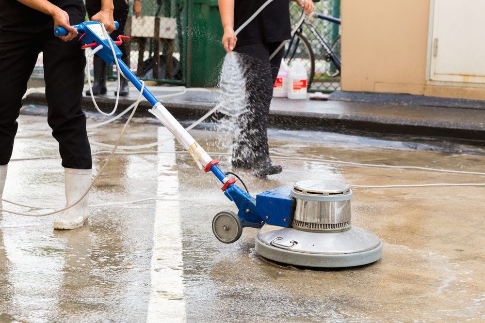 A Person Is Using a Machine to Clean a Concrete Floor — North Coast Commercial Cleaners In Bli Bli, QLD