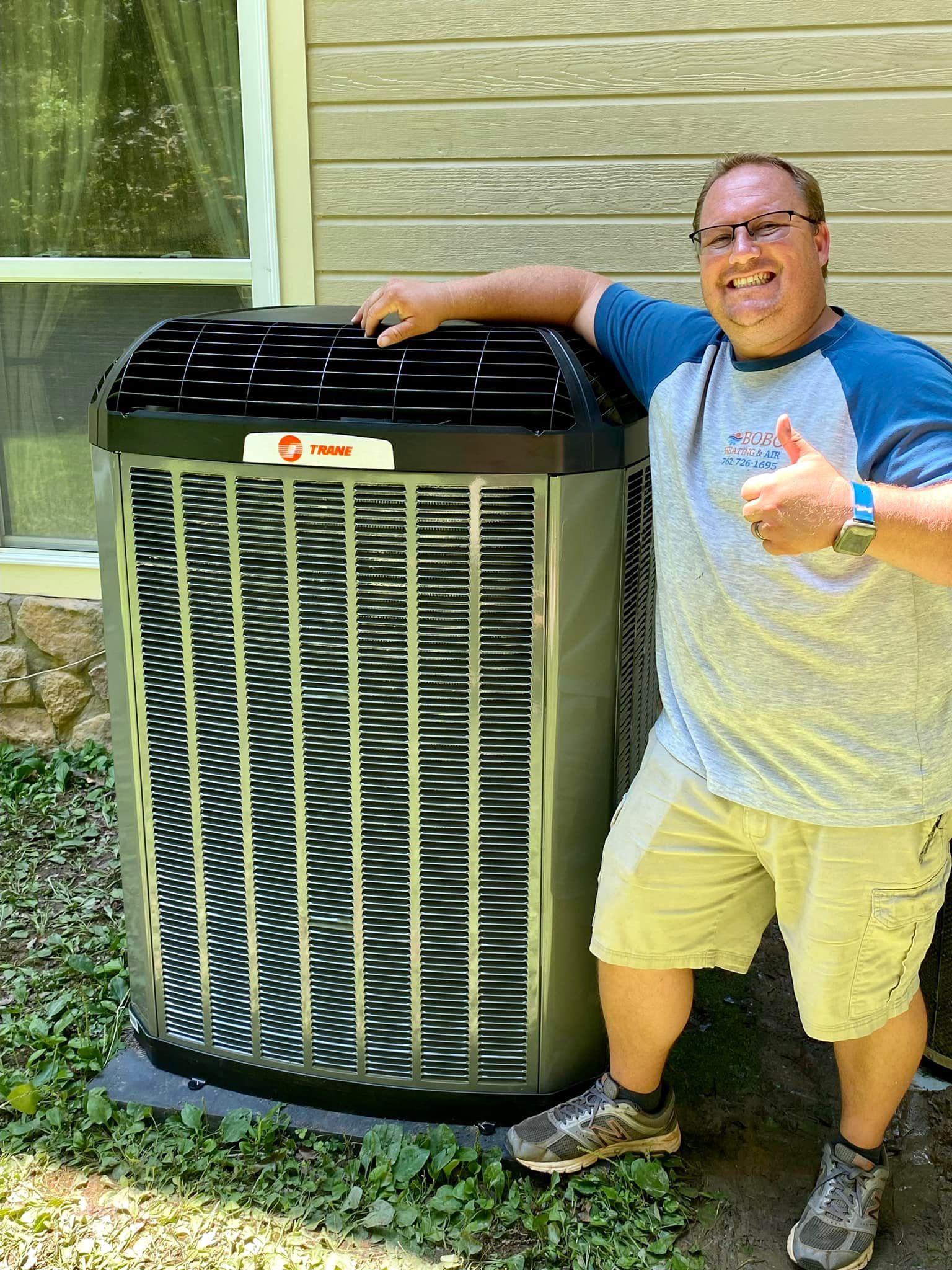 Man thumbs up next to new Trane air conditioner unit outdoors.