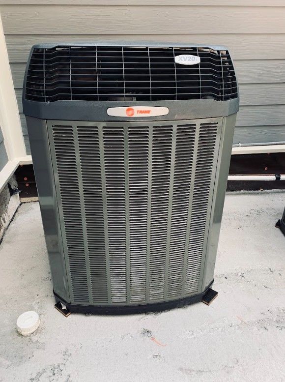 Gray Trane air conditioner unit on a concrete surface next to a building.