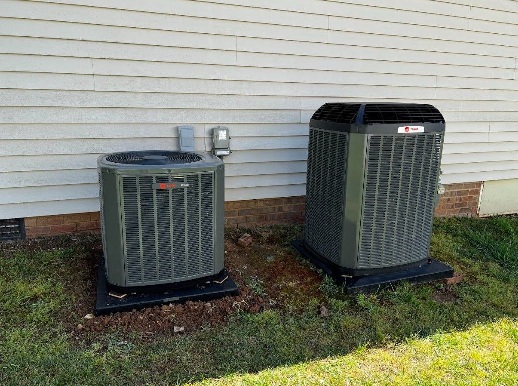 Two outdoor air conditioning units on black pads next to a white house.