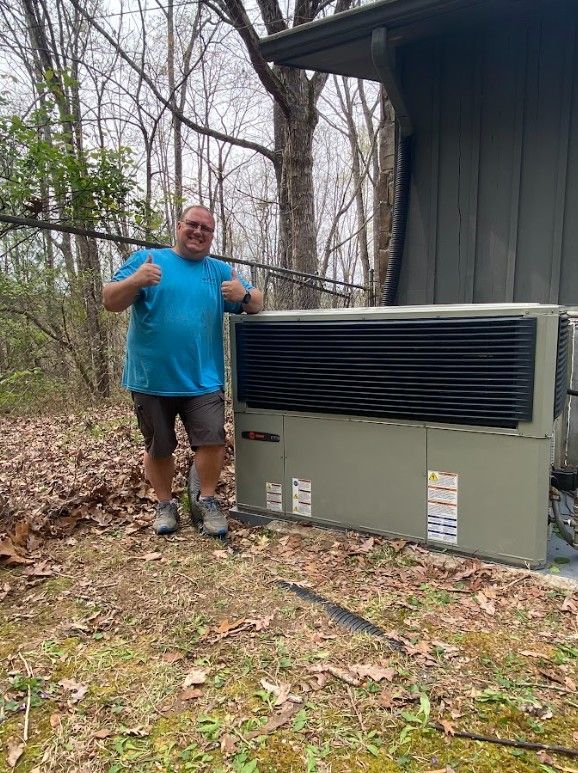Man in a blue shirt gives thumbs up next to a new outdoor HVAC unit.