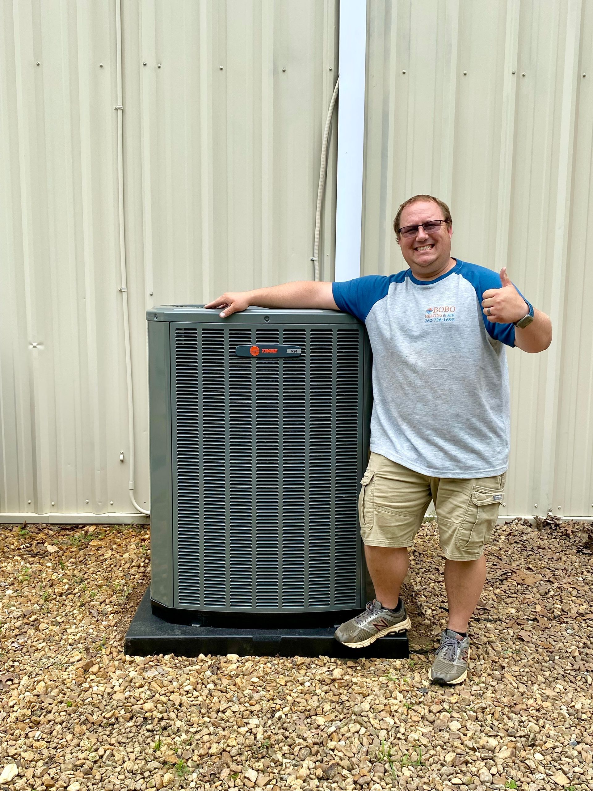 Man giving thumbs up next to new HVAC unit outside a building.