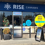 Exterior of a RISE Cannabis store with an open sign and happy hour promotion.