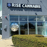 Exterior of Rise Cannabis dispensary, gray building with large windows and sign, open.