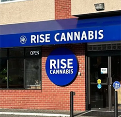 Exterior of a Rise Cannabis store with blue and white signage. The building is brick.