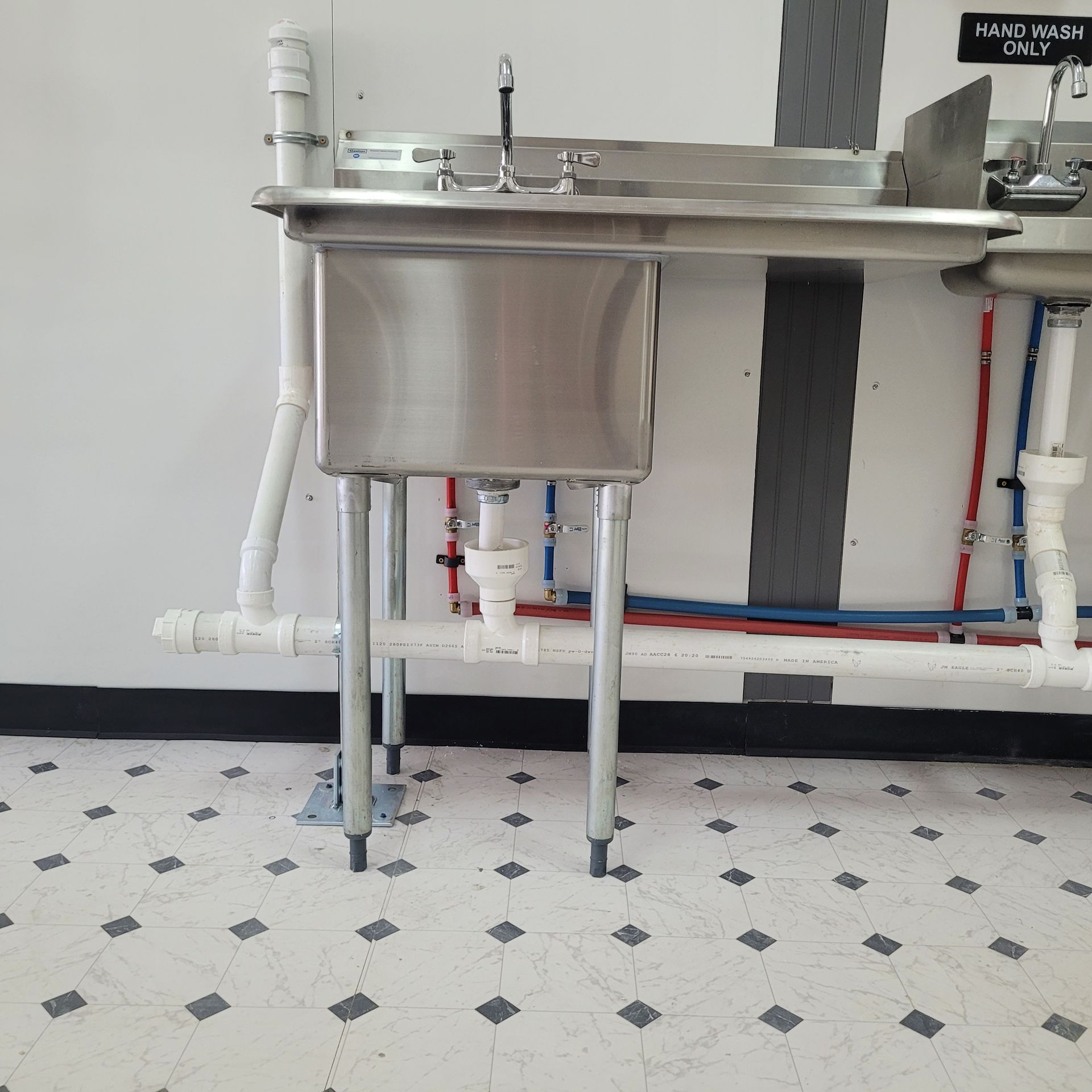 A stainless steel sink in a kitchen with a sign on the wall that says hand washing only