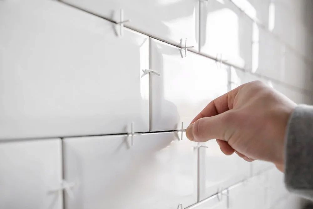 Hand Placing Tile Spacer Between White Subway Tiles on a Wall — Corrimal Ceramic Tiles Pty Ltd in Corrimal, NSW