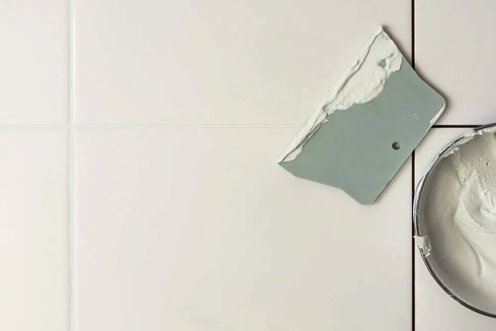 A Spatula Is Laying On A Tile Next To A Bowl Of Grout — Corrimal Ceramic Tiles Pty Ltd in Gerringong, NSW