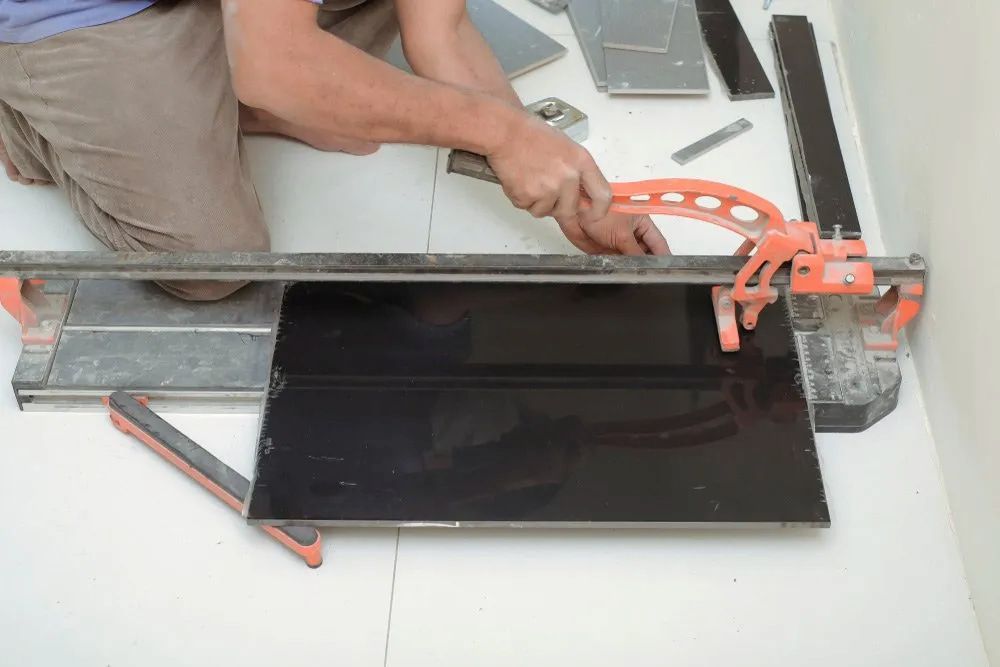 A Man Is Cutting A Tile With A Tile Cutter — Corrimal Ceramic Tiles Pty Ltd in Corrimal, NSW