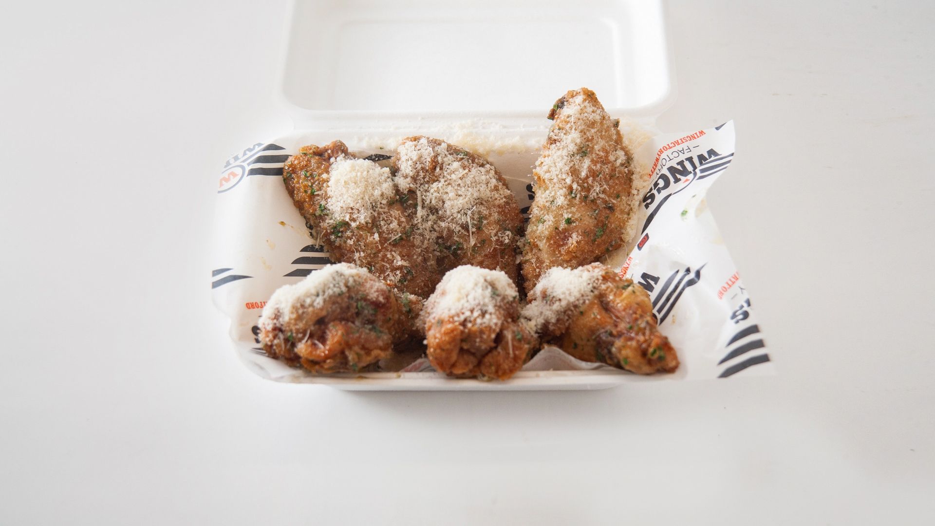 A styrofoam container filled with fried chicken wings covered in powdered sugar.