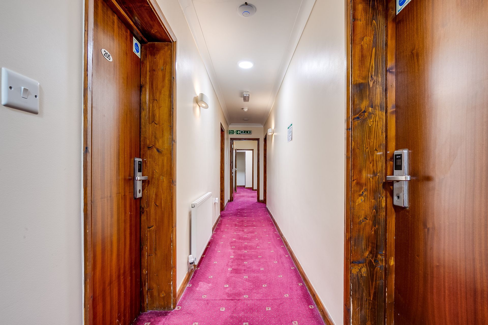 A long hallway with a pink carpet and wooden doors.