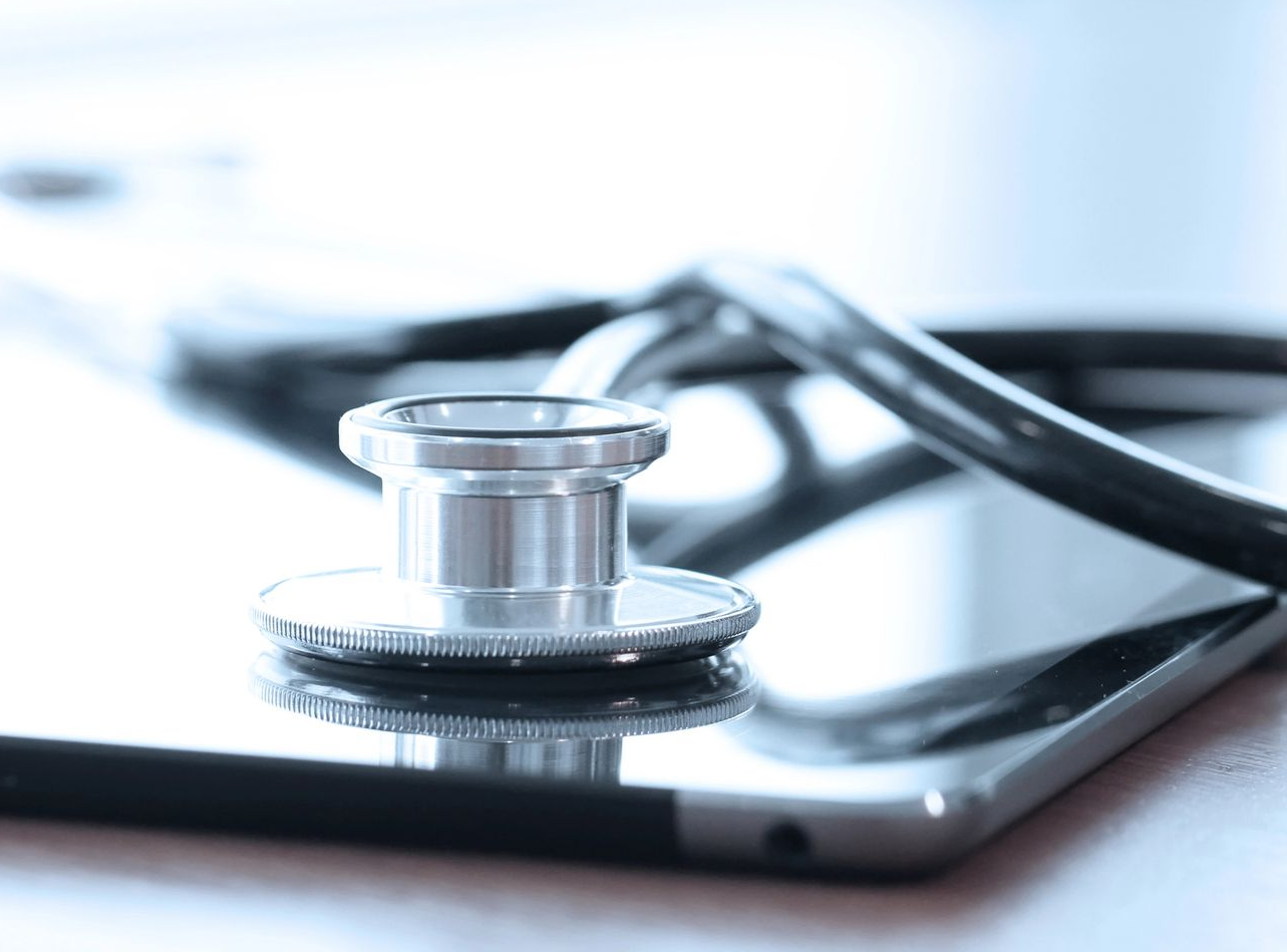 Uno stetoscopio argentato appoggiato sullo schermo scuro e riflettente di un tablet.
