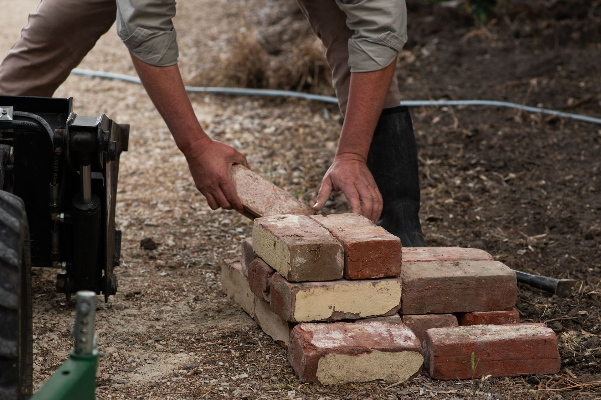 ‘’Person stacking red and beige bricks on a dirt ground’’ ‘’Person stacking red and beige bricks on a dirt ground’’