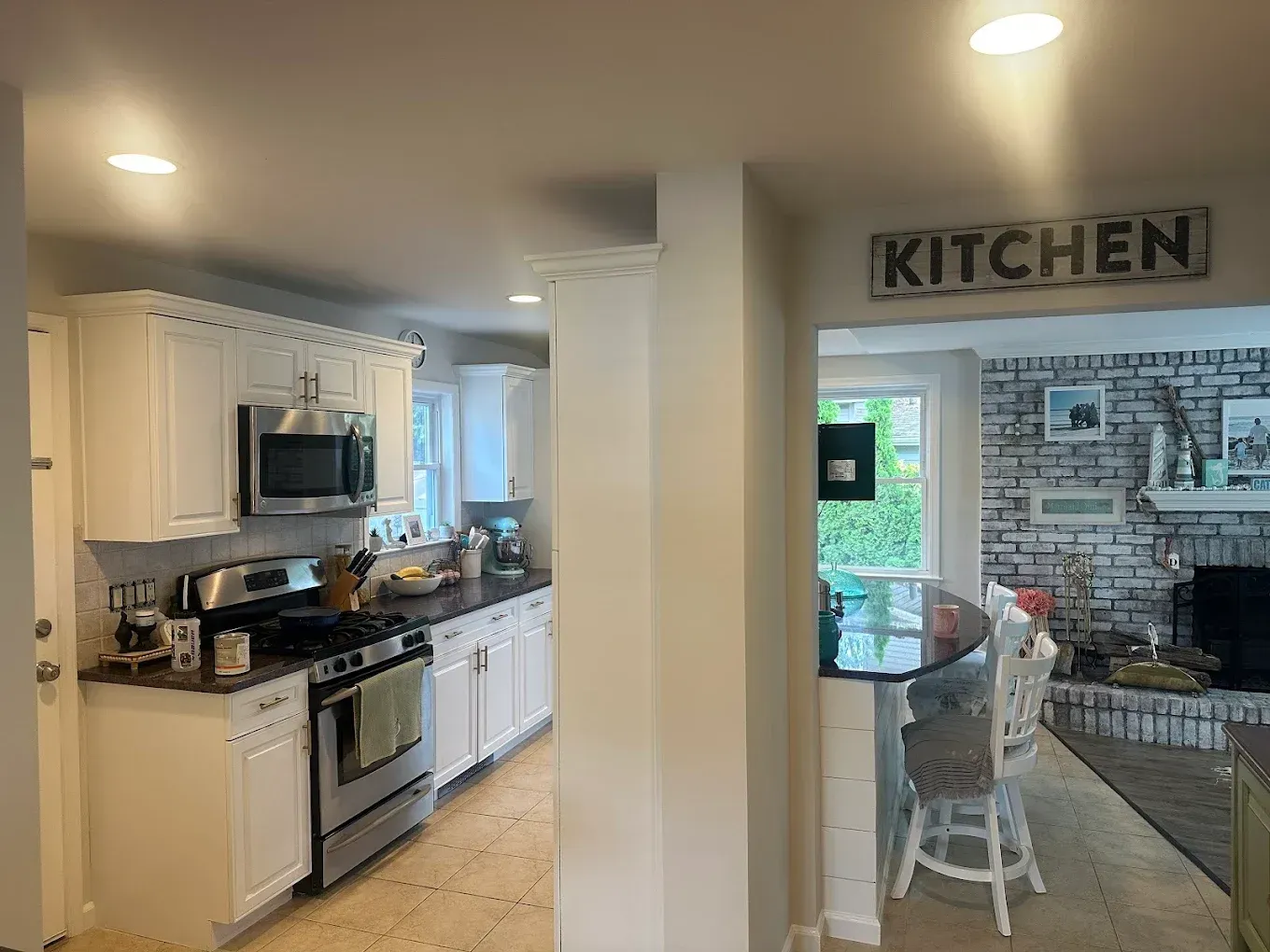 Open kitchen with white cabinets, stainless stove, and a view into a living room with a brick fireplace.