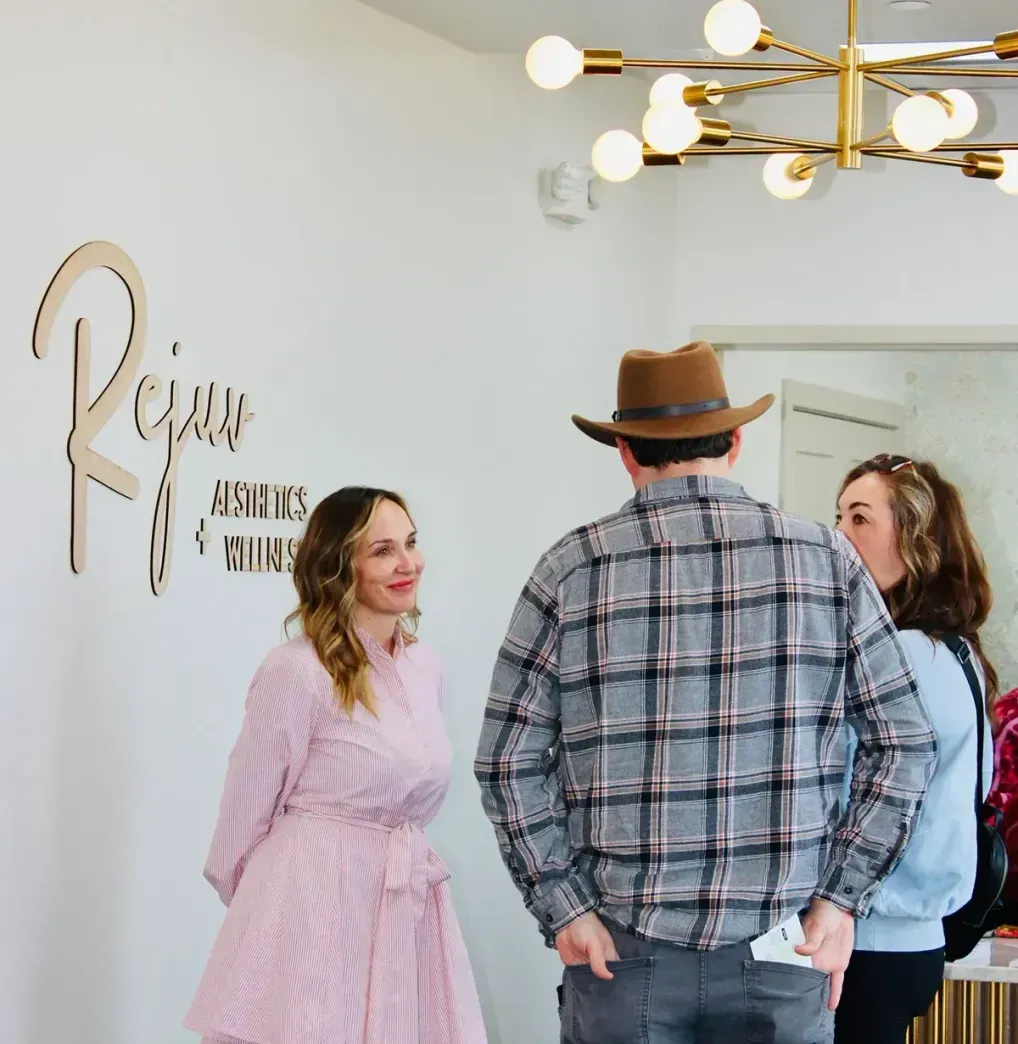A person in a pink dress smiles as they talk with two others standing near a wall sign reading