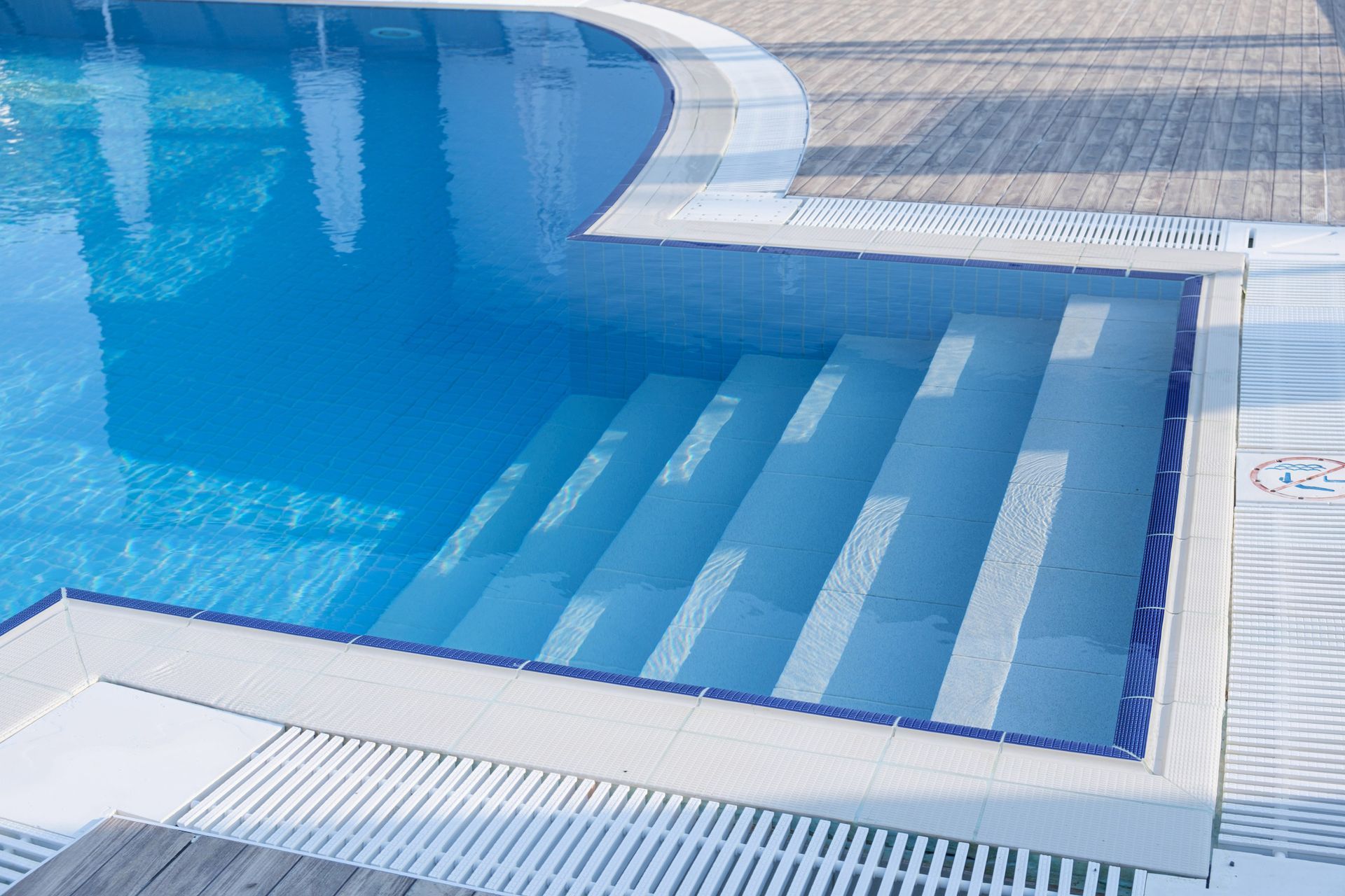 Pool with blue water and white steps. The pool's edge has a white border, and the steps descend into the water.