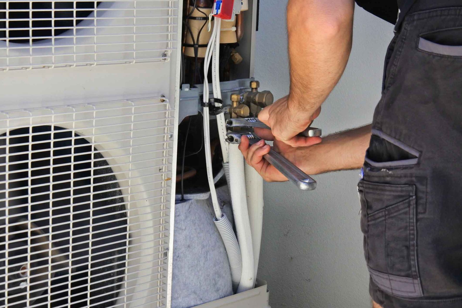 A man is working on an air conditioner with a wrench.