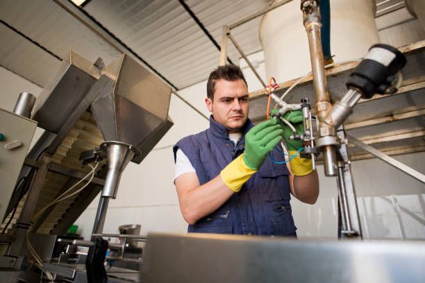A man wearing green gloves is working on a machine in a factory.