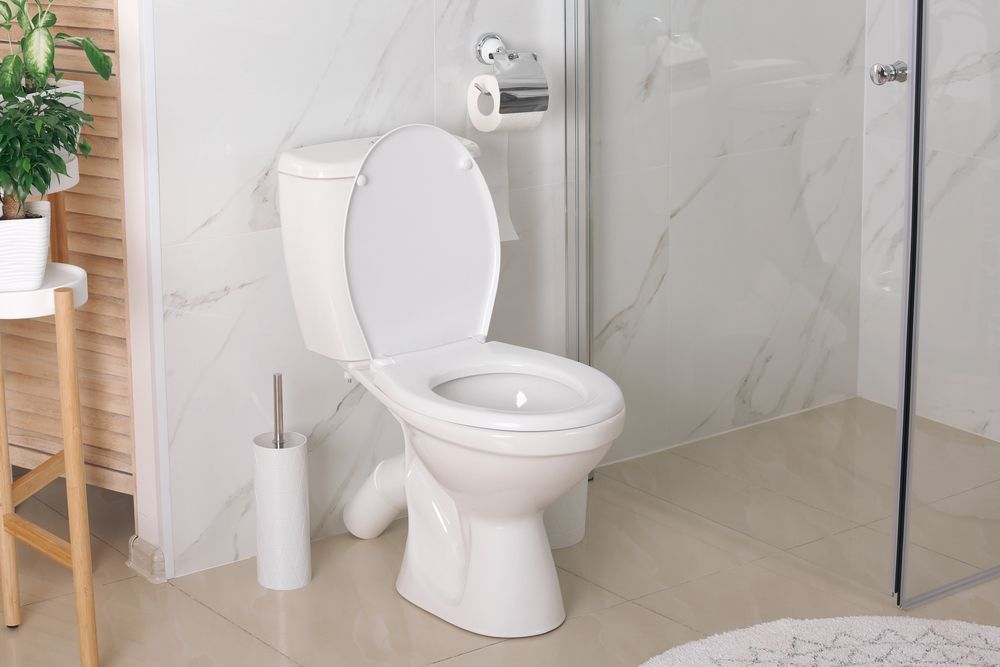 White toilet with an open lid in a modern bathroom with marble walls and a shower.