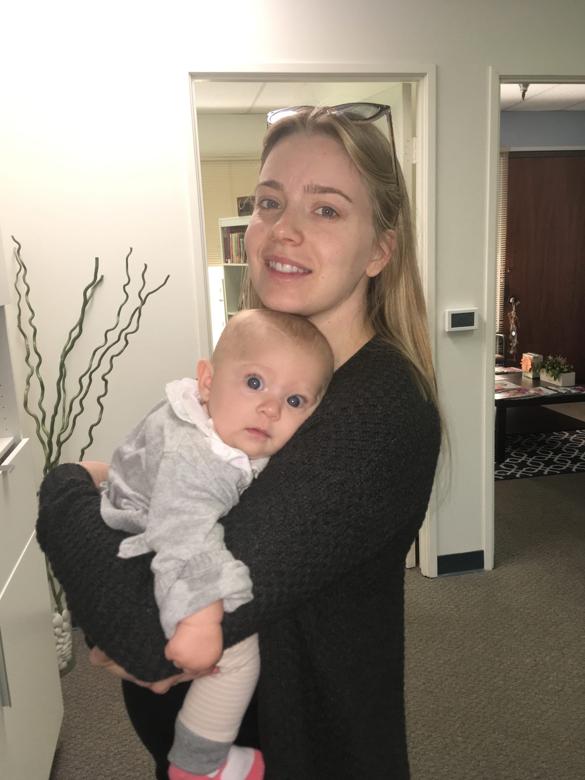 Woman holding a baby in an office. The baby is wearing grey with pink socks.