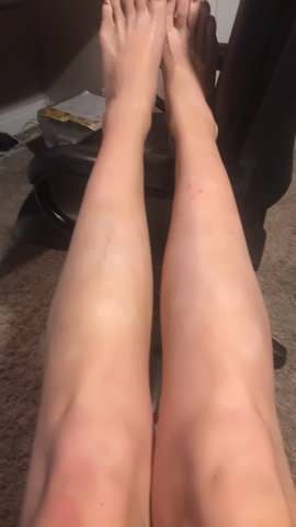 Bare legs, knees bent, lying down with feet pointing up; indoor setting with dark furniture.