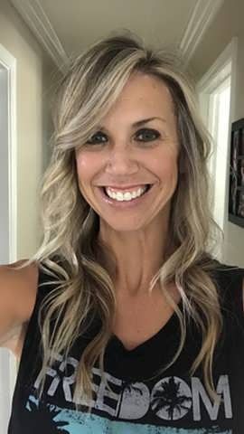 Woman with blonde hair smiling, wearing a black tank top that says