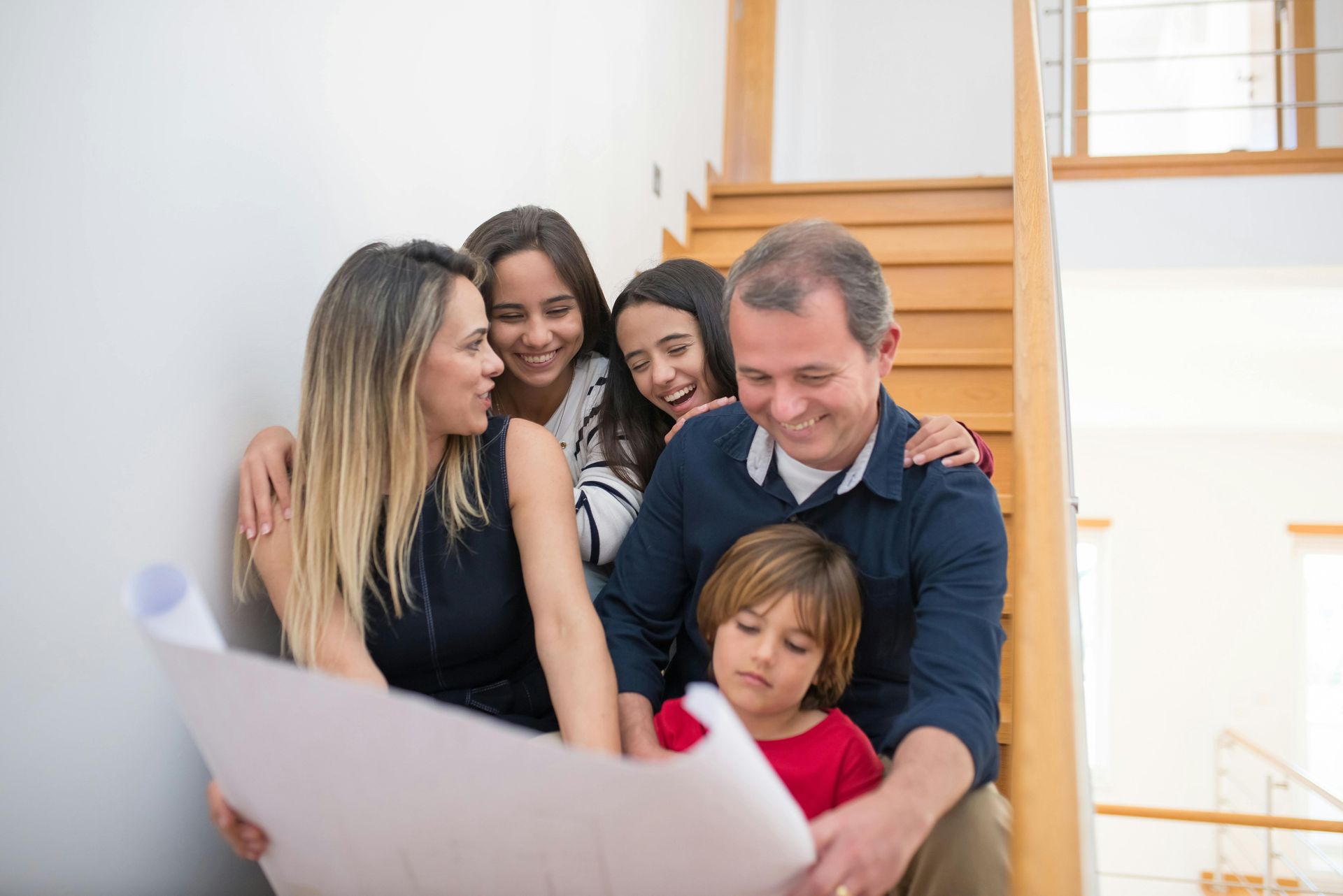 Family gathered around a staircase, smiling and looking at a large paper plan or drawing.