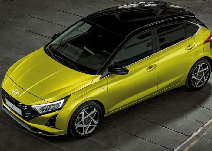 A yellow car with a black roof is parked in a parking lot. i20