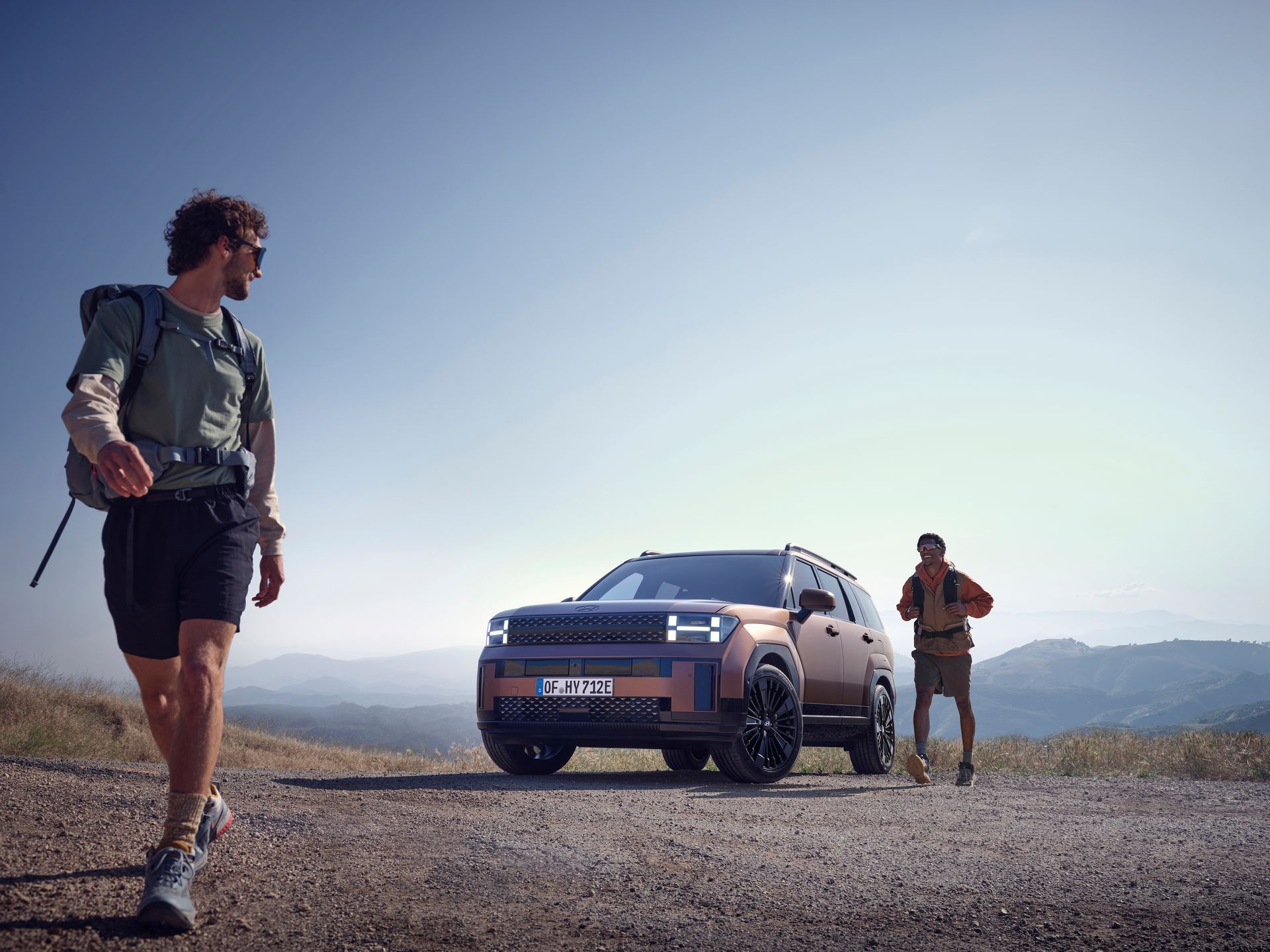 Two men are walking next to a car on a dirt road.
