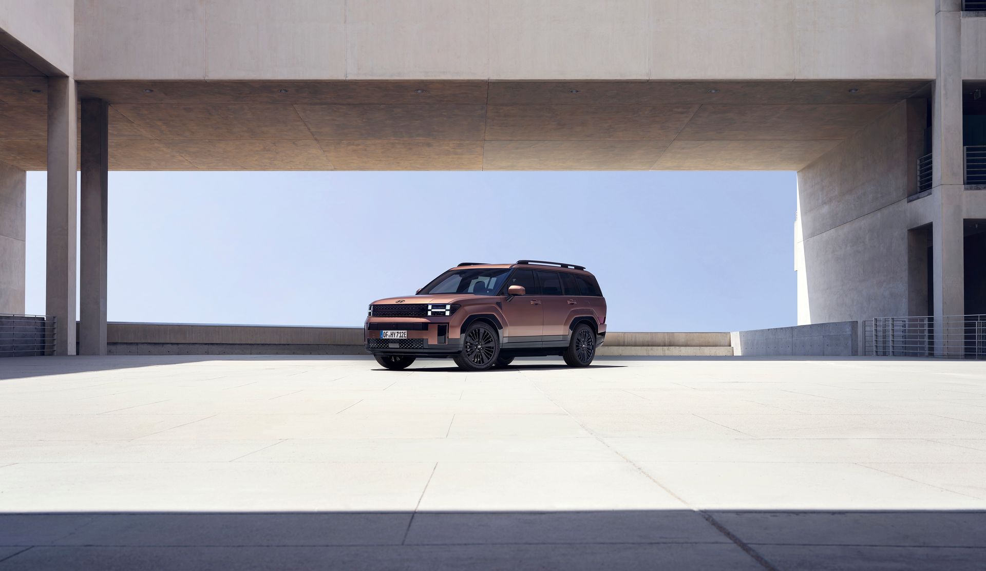 A brown suv is parked under a bridge in a parking lot.