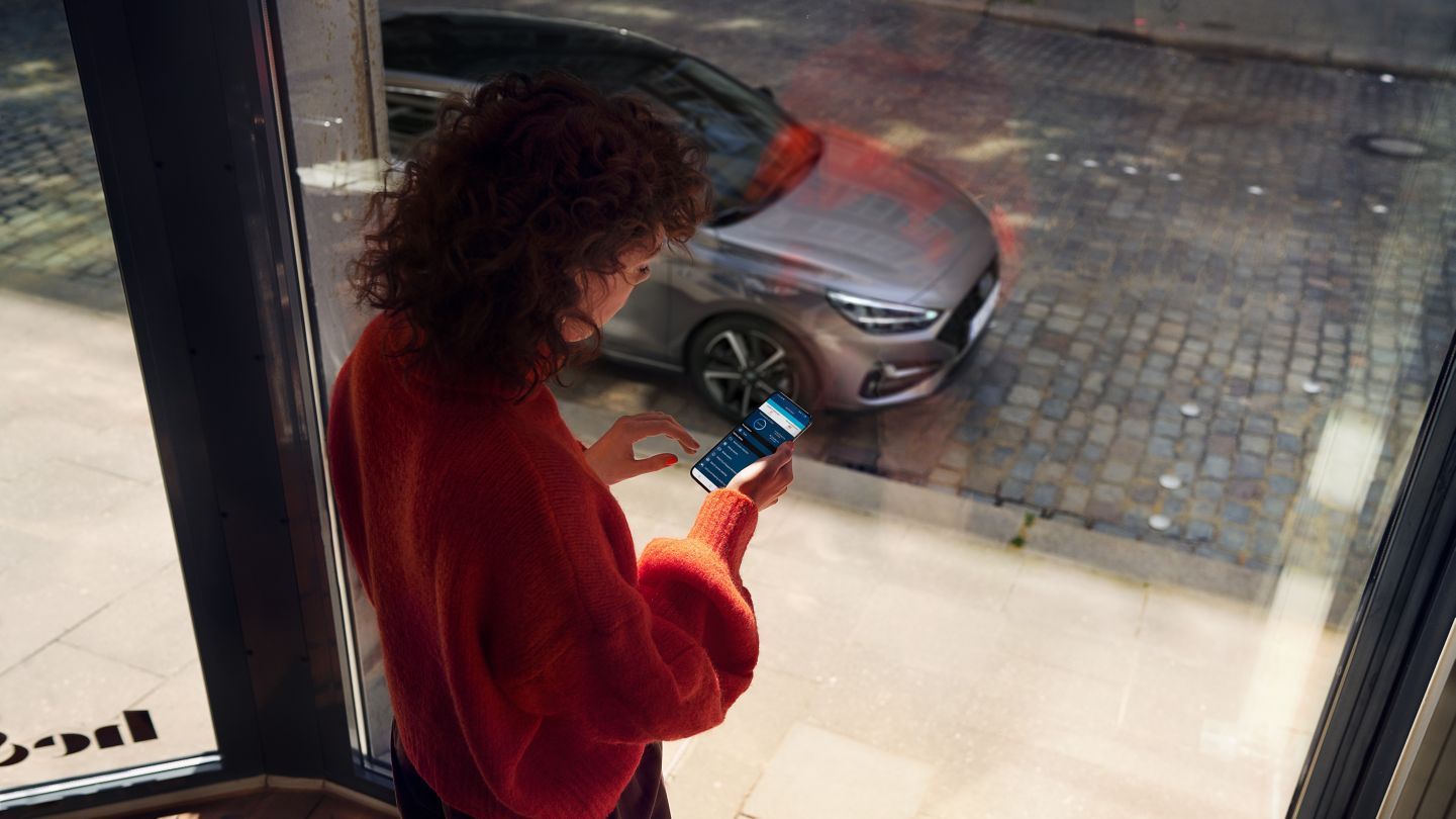 A woman is standing in front of a window looking at her phone. i30