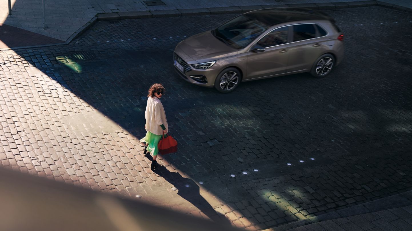 A woman is walking down a cobblestone street next to a car. i30