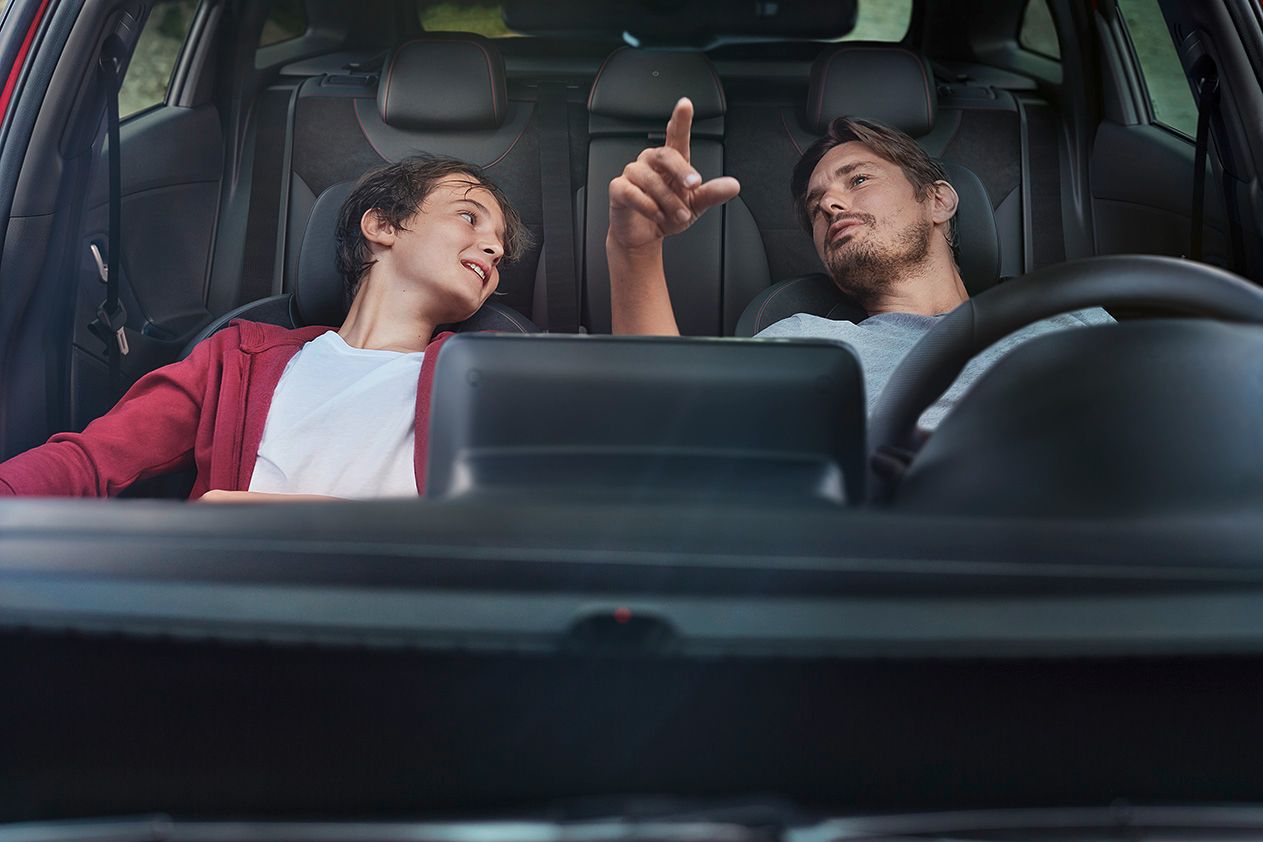 Two men are sitting in the back seat of a car looking at a tablet. i30