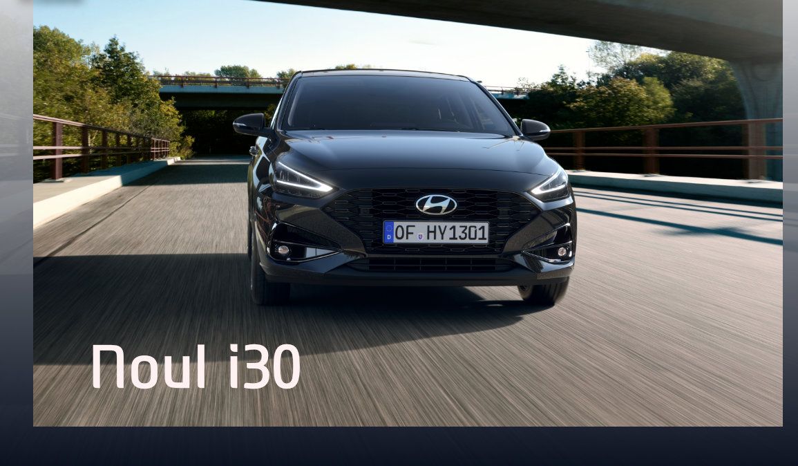 A black hyundai car is driving down a road under a bridge.