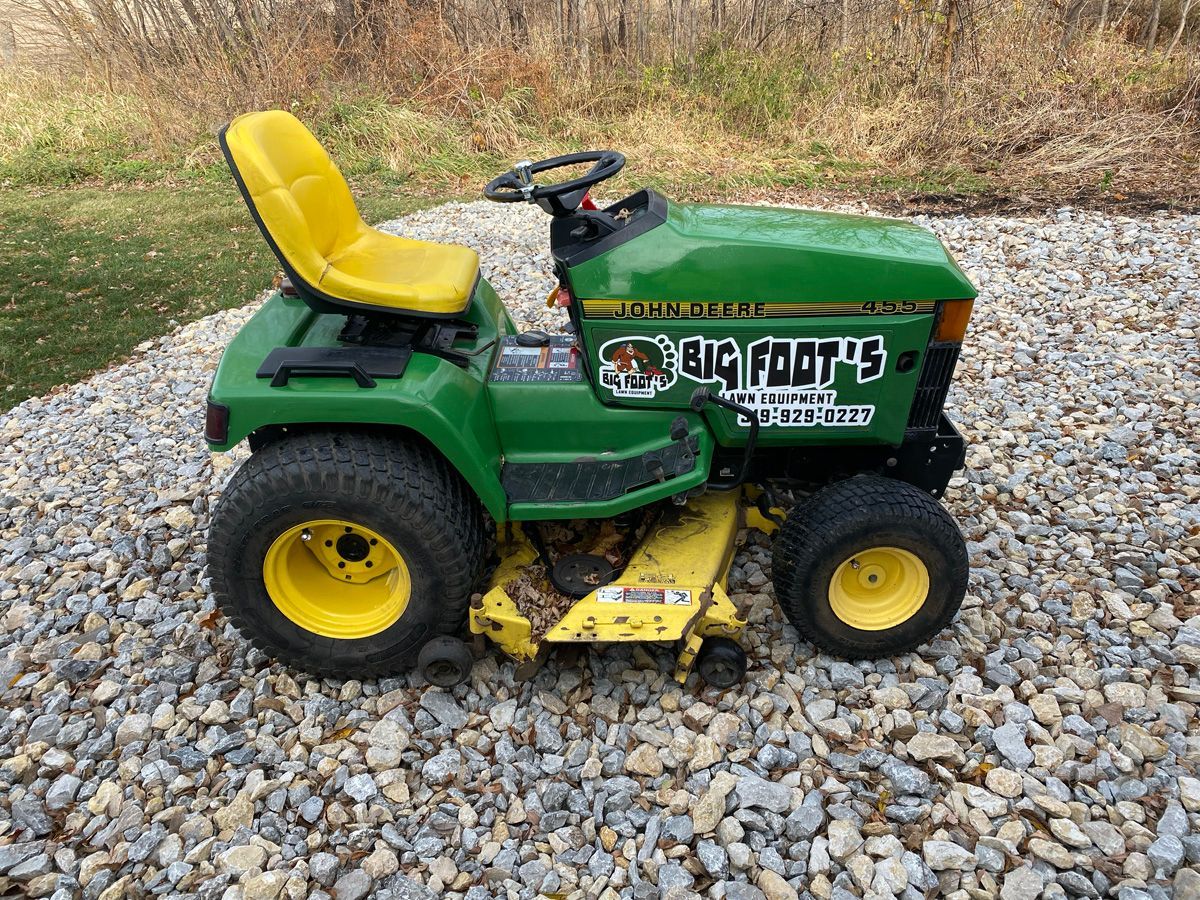A green and yellow john deere lawn mower is parked on a gravel road.