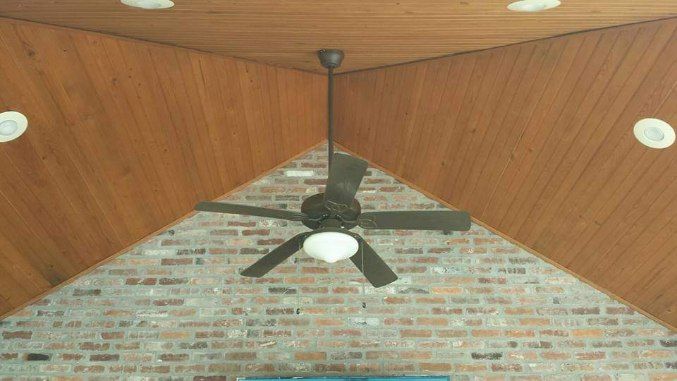 A ceiling fan is hanging from the ceiling of a room with a brick wall.