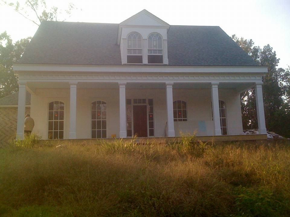 A large white house with a porch is surrounded by tall grass