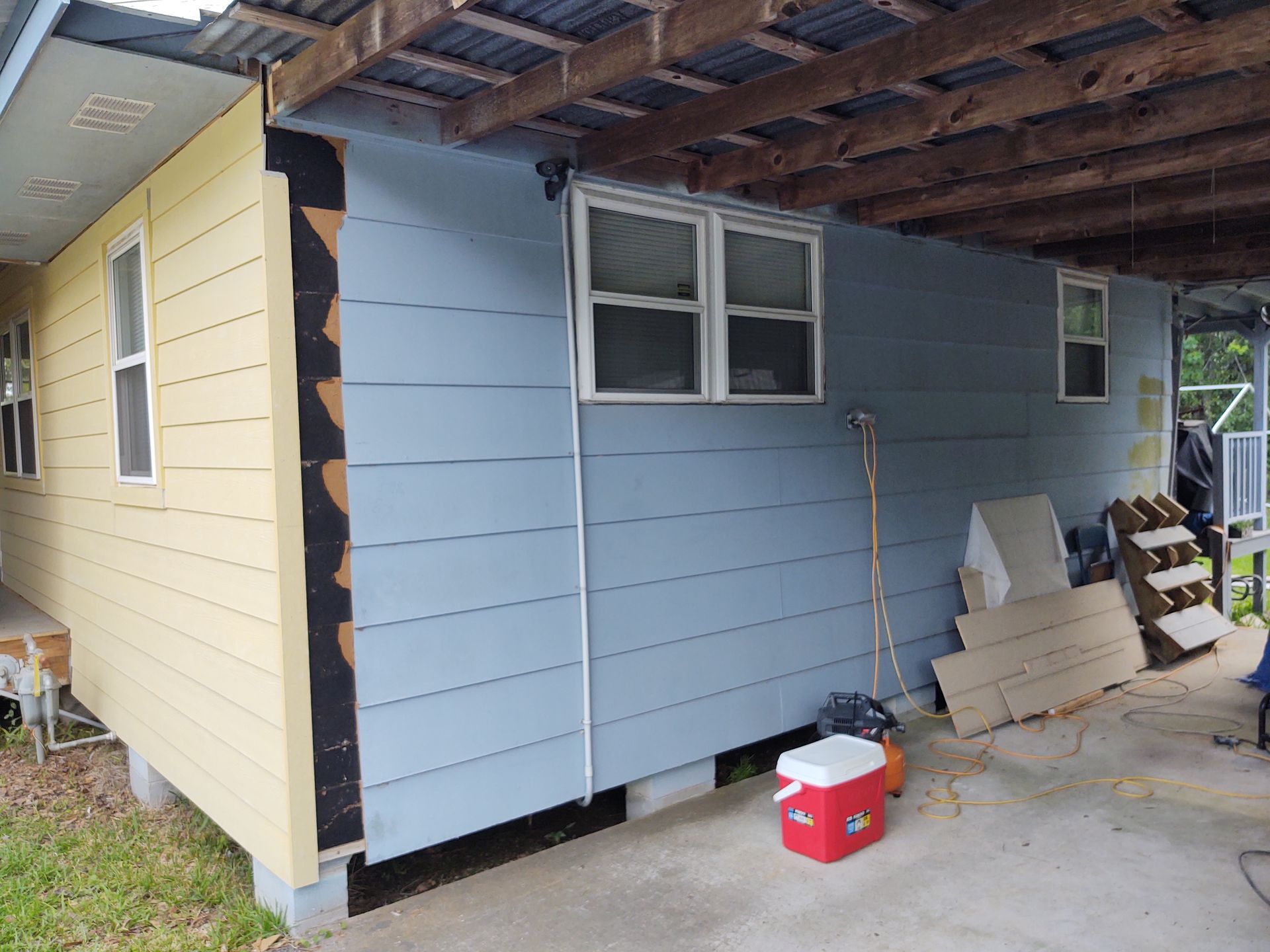 A blue and yellow house with a red cooler in front of it